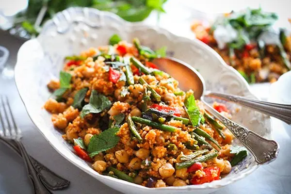 Gemüse-Couscous mit Zitronen-Minz-Joghurt auf einem Teller. Schnelles, veganes Couscous-Gericht