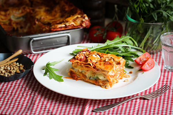 Ein Stück kross überbackene vegane Lasagne auf einem Teller und rot-weißer Tischdecke
