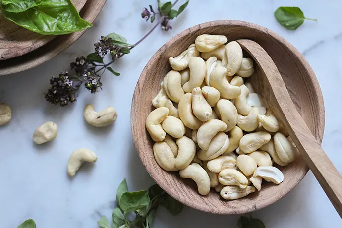 Cashewnüsse in einer Holzschale auf einem weißen Marmortisch mit Kräutern