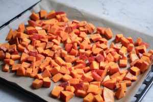 Gewürfelter Hokkaido-Kürbis mit Kokosöl und Zimt vermischt auf einem Backblech (Herstellung Kürbispürée)