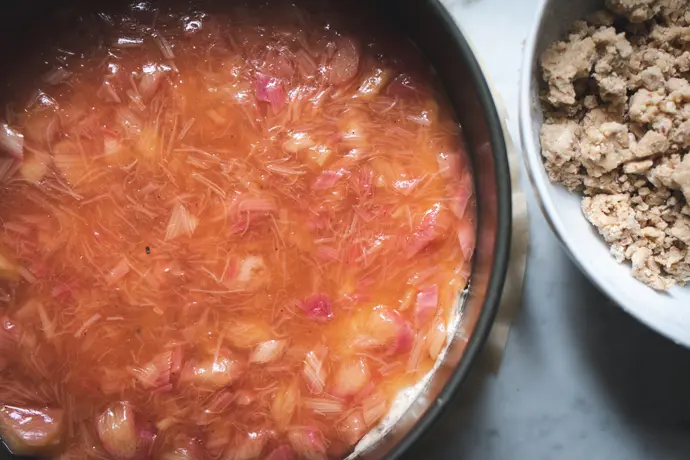 Zubereitung eines veganen Rhabarberkuchens. Fruchtschicht wird auf Kuchenboden aufgetragen