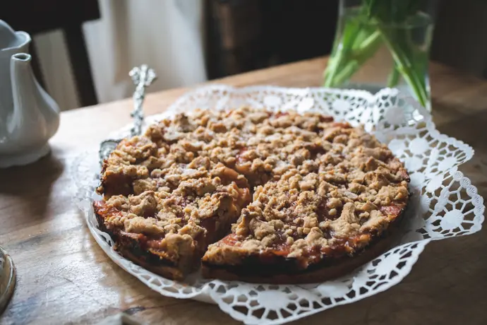 Veganer Rhabarber-Streuselkuchen auf einem rustikalen Holztisch, angeschnitten