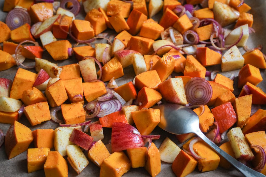 Geröstete Kürbis- und Apfelstücke mit Zwiebeln auf einem Backblech