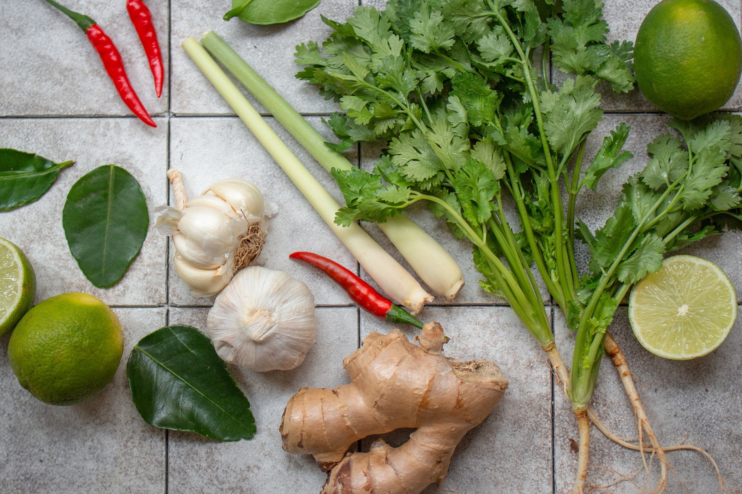 Ingwerwurzel, frischer Koriander, Zitronengras, Chilischoten und Kaffir-Limettenblätter auf einer Arbeitsfläche