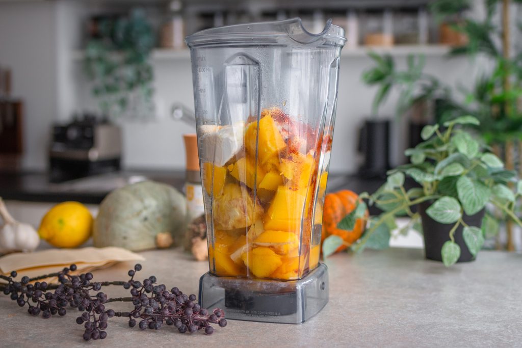 Herstellung einer Kürbissoße für Kürbislasagne. Alle Zutaten sind in einem Mixbehälter zu sehen.