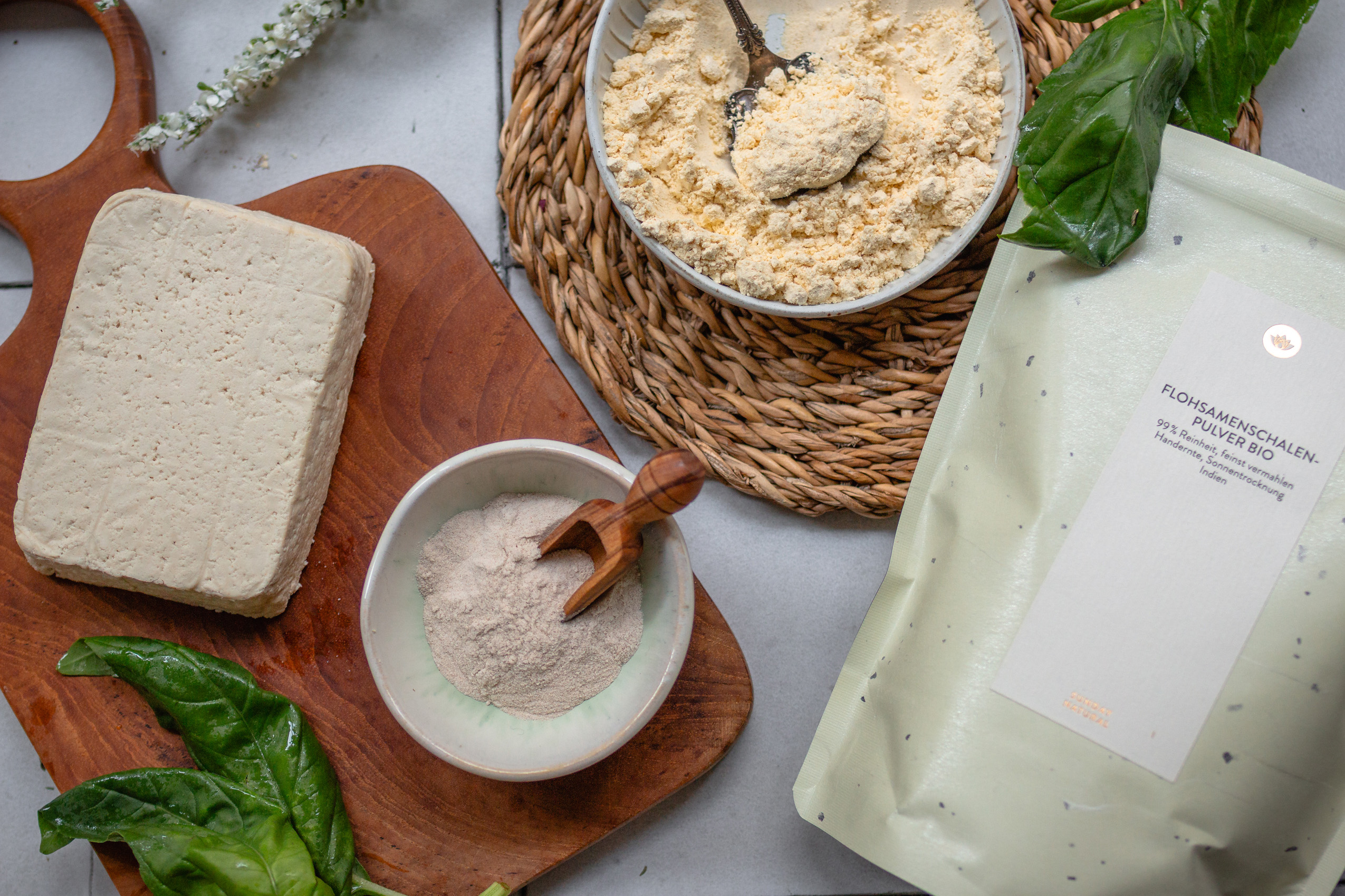 Auf einer Arbeitsfläche sieht man einen Block Naturtofu, Kichererbsenmehl und gemahlene Flohsamenschalen
