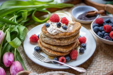 Weiche, vegane Skyr-Pancakes mit Beeren, gestapelt auf einem frühlingshaft gedecktem Tisch