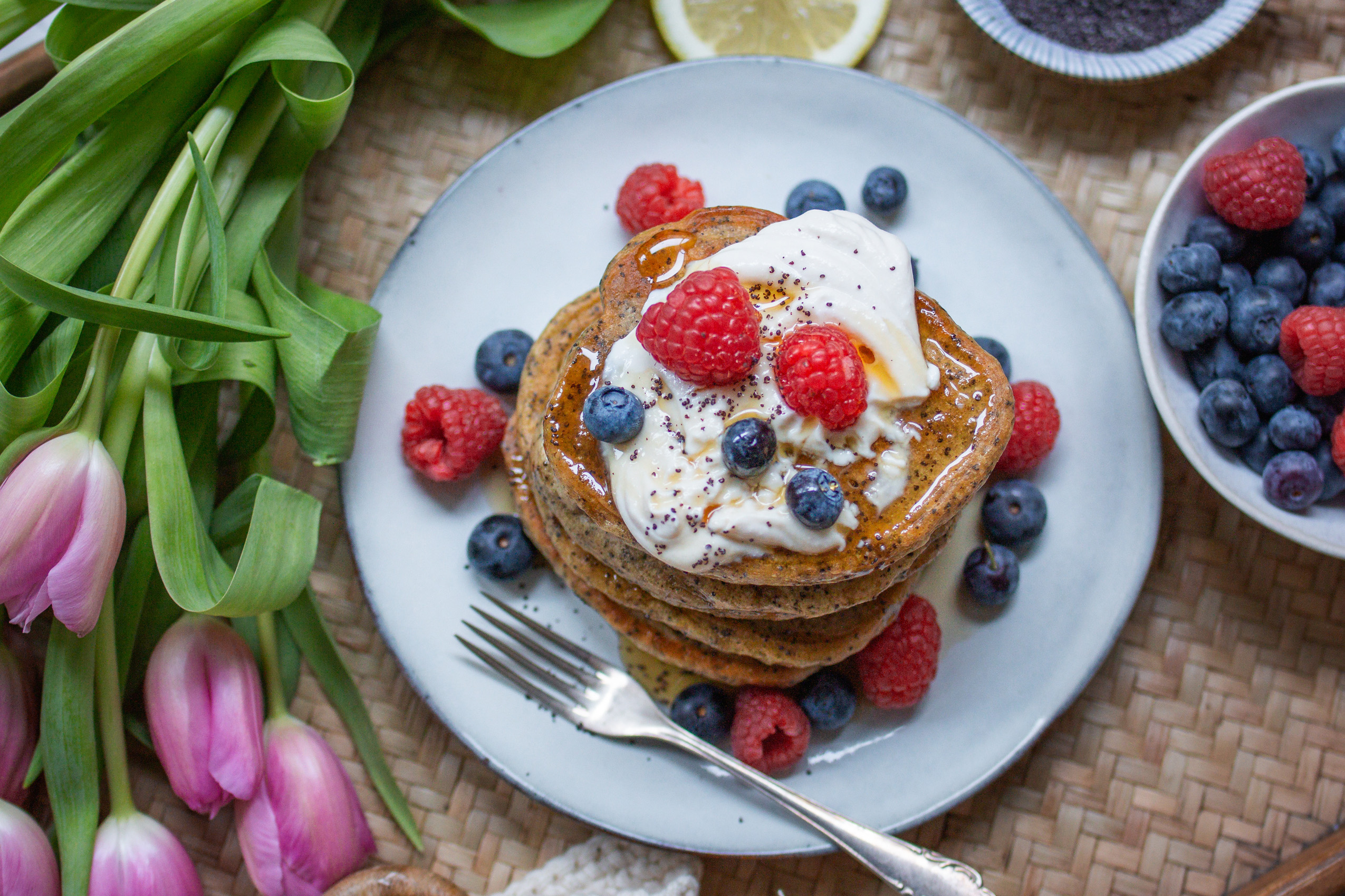 Vegane Skyr-Pancakes mit Beren und Ahornsirup auf einem teller gestapelt und frühlingshaft dekoriert