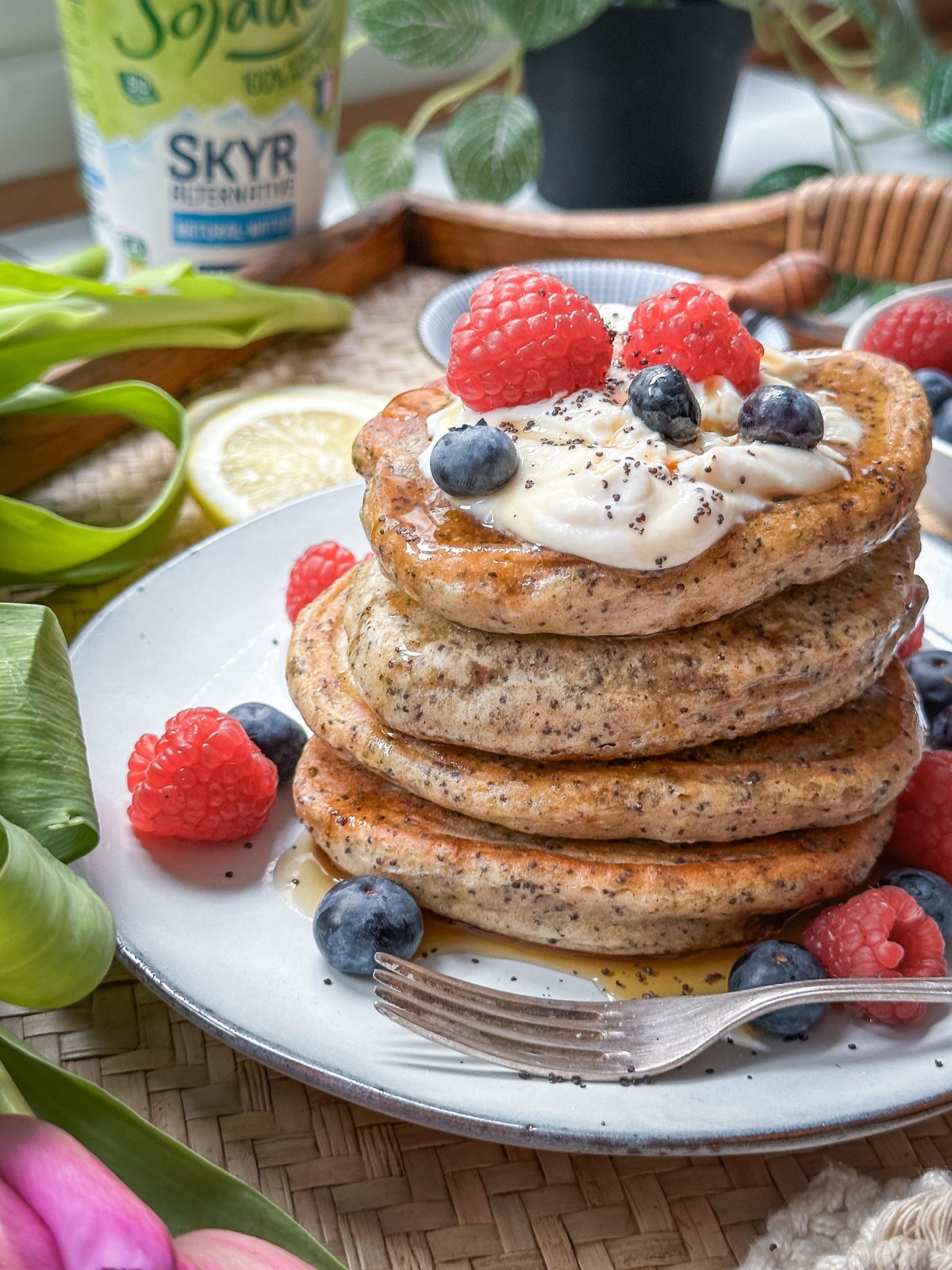 Vegane Zitronen-Mohn-Pancakes gestapelt und mit Ahornsirup und Beeren garniert