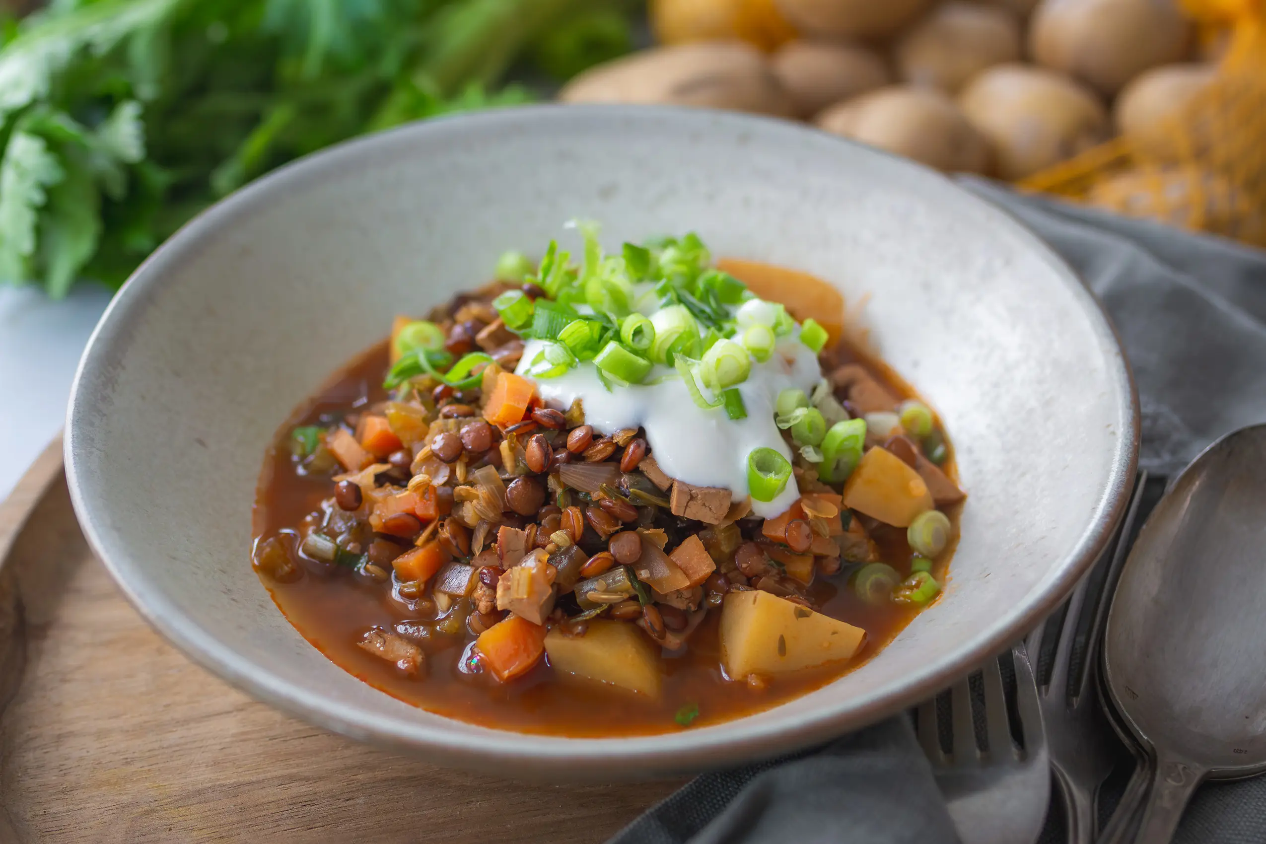 Veganer Berglinseneintopf mit Wurzelgemüse in einer Schale auf einem Tisch mit Kartoffeln und Sellerie im Hintergrund