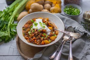 Veganer Berglinseneintopf angerichtet mit Joghurt und Frühlingszwiebeln