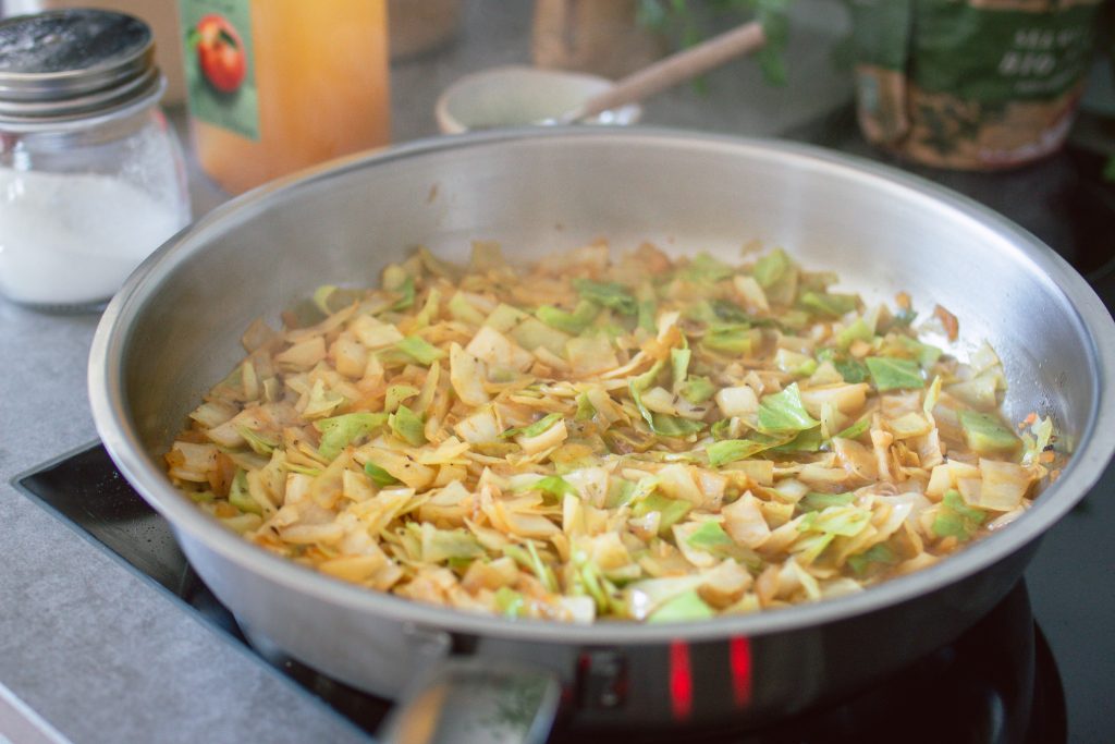 Weißkraut und zwiebeln werden in einer Pfanne goldbraun geswchmort, um Krautfleckerl zuzubereiten