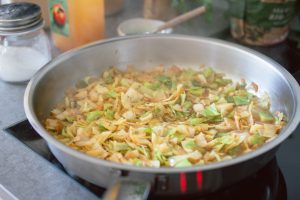Weißkraut und zwiebeln werden in einer Pfanne goldbraun geswchmort, um Krautfleckerl zuzubereiten